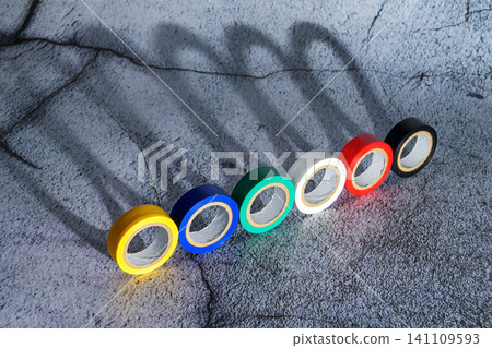 rolls of colored electrical tape stand on edge in a row diagonally on a concrete gray surface rolls of colored electrical tape stand on edge in a row diagonally on a concrete gray surface 141109593