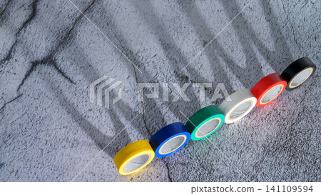 multicolored insulating tape lies on a gray background diagonally with shadows from leaves multicolored insulating tape lies on a gray background diagonally with shadows from leaves 141109594