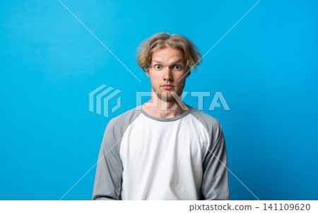 Young man showing a wide-eyed and surprised facial expression, capturing the emotion of shock, astonishment, or disbelief against a vibrant blue studio background Young man showing a wide-eyed and surprised facial expression, capturing the emotion of shock, astonishment, or disbelief against a vibrant blue studio background 141109620
