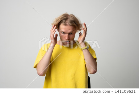 Young blond man experiencing shock and disbelief, reacting to unexpected news or a surprising event with wide eyes and hands near his head, expressing frustration Young blond man experiencing shock and disbelief, reacting to unexpected news or a surprising event with wide eyes and hands near his head, expressing frustration 141109621