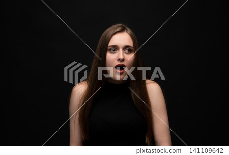 Young woman having an unexpected shocking reaction, expressing surprise and sudden fear looking away on dark background Young woman having an unexpected shocking reaction, expressing surprise and sudden fear looking away on dark background 141109642