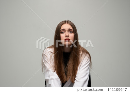 Young woman feeling sad and tired, sitting in a studio, looking at the camera with a deflated expression Young woman feeling sad and tired, sitting in a studio, looking at the camera with a deflated expression 141109647