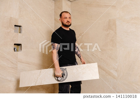 Tiler installing large format tile on bathroom wall using suction cup Tiler installing large format tile on bathroom wall using suction cup 141110018