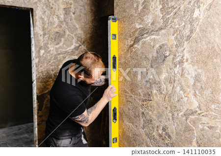 Construction worker using spirit level installing marble tile on wall Construction worker using spirit level installing marble tile on wall 141110035