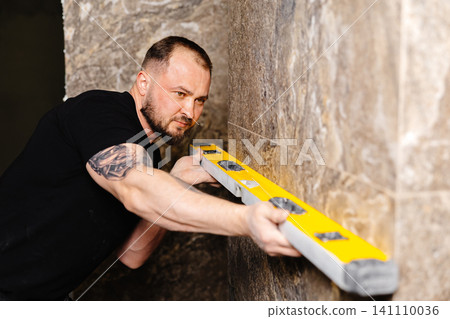 Construction worker using spirit level installing marble tile on wall Construction worker using spirit level installing marble tile on wall 141110036