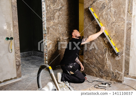 Construction worker using spirit level installing marble tile on wall Construction worker using spirit level installing marble tile on wall 141110037
