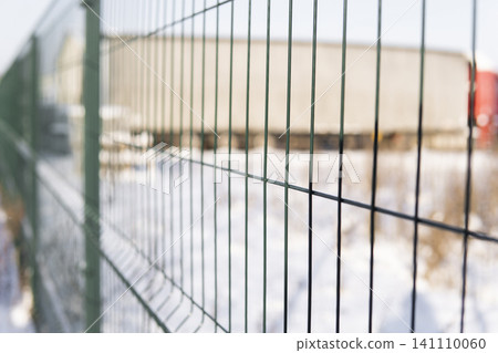 Green wire mesh fence bordering an industrial area in winter, providing security and showing restrictions Green wire mesh fence bordering an industrial area in winter, providing security and showing restrictions 141110060