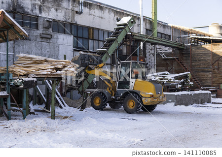 Wood processing facility operating in winter, industrial loader moving wood chips onto a conveyor belt system Wood processing facility operating in winter, industrial loader moving wood chips onto a conveyor belt system 141110085