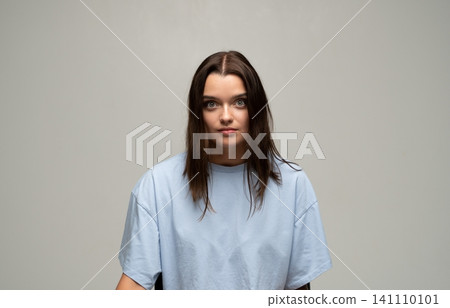 Young woman with brown hair and light blue t-shirt posing in studio, having a neutral and serious expression Young woman with brown hair and light blue t-shirt posing in studio, having a neutral and serious expression 141110101