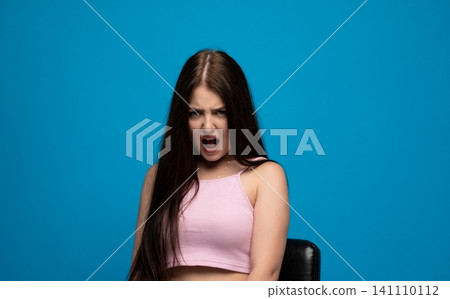 Young woman shouting and expressing frustration, anger, and aggression with mouth open on blue background Young woman shouting and expressing frustration, anger, and aggression with mouth open on blue background 141110112