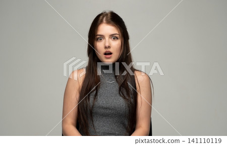 Young woman reacting with open mouth and wide eyes, expressing surprise, shock, and disbelief looking at camera 141110119