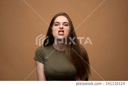 Young woman grimacing, expressing anger, frustration, and disgust, clenching teeth in a confrontational emotion Young woman grimacing, expressing anger, frustration, and disgust, clenching teeth in a confrontational emotion 141110124