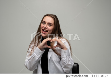 Young woman smiling with open mouth, showing a heart shape with her hands, conveying love, care, and happiness Young woman smiling with open mouth, showing a heart shape with her hands, conveying love, care, and happiness 141110126