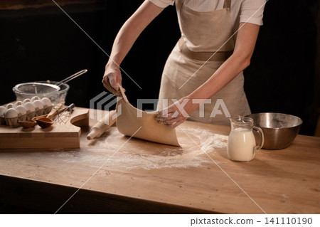 Baker hands stretching fresh dough on rustic wooden table, preparing homemade pastry with flour and eggs Baker hands stretching fresh dough on rustic wooden table, preparing homemade pastry with flour and eggs 141110190