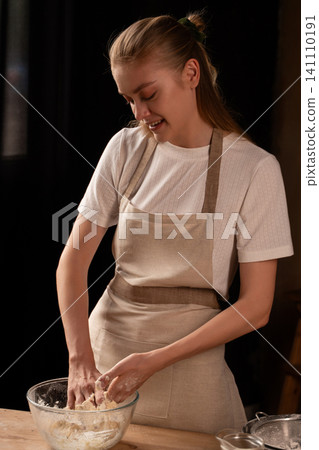 Young woman enjoying kneading dough in a glass bowl, creating handmade bread or pastry in a home kitchen setting 141110191