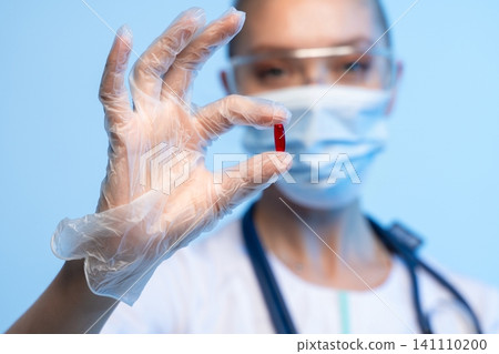 Doctor or nurse in personal protective equipment holding a red pill, representing medical treatment, health, and research Doctor or nurse in personal protective equipment holding a red pill, representing medical treatment, health, and research 141110200
