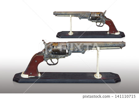 side view two antique and old brass guns with a brown leather grip, placed on a wooden stand against a white background 141110715