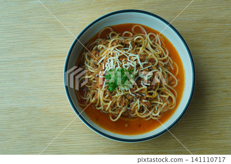 top view Pork spaghetti garnished with vegetables and a cheese slice, served in a white ceramic bowl with a black rim and placed on a wooden table top view Pork spaghetti garnished with vegetables and a cheese slice, served in a white ceramic bowl with a black rim and placed on a wooden table 141110717