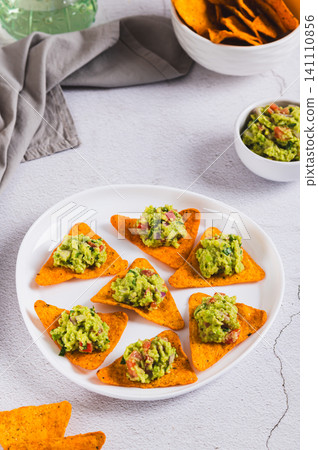 Delicious avocado guacamole on nacho chips on a plate on the table vertical view 141110856