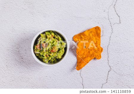 Delicious avocado guacamole in a bowl and some nacho chips on the table top view Delicious avocado guacamole in a bowl and some nacho chips on the table top view 141110859
