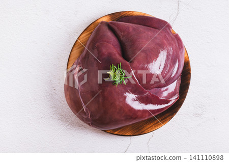 Close up of raw whole pork liver on a wooden board on the table top view Close up of raw whole pork liver on a wooden board on the table top view 141110898