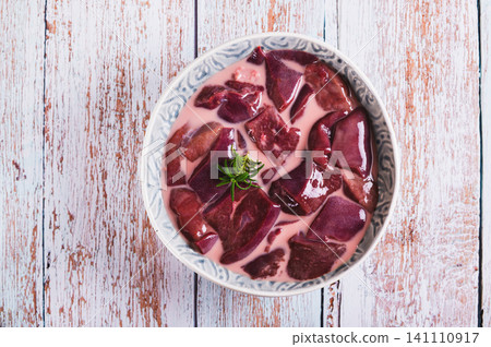 Close up of raw pork liver soaked in milk in a bowl on the table top view 141110917