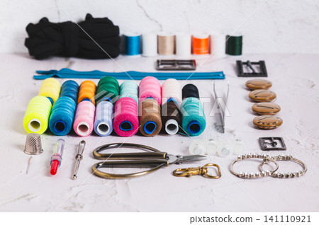 A set of spools of multi-colored threads and sewing supplies on a table A set of spools of multi-colored threads and sewing supplies on a table 141110921