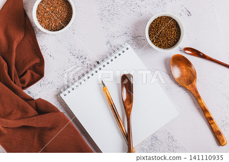Close up of a notebook and pen for writing down recipes, spoons and spices on the kitchen table top view 141110935