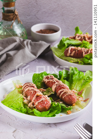 Grilled sausage with sauce and croutons on lettuce leaves on a plate on the table vertical view Grilled sausage with sauce and croutons on lettuce leaves on a plate on the table vertical view 141110951