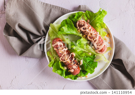 Close up of grilled sausage with sauce and croutons on lettuce leaves on a plate on the table top view Close up of grilled sausage with sauce and croutons on lettuce leaves on a plate on the table top view 141110954