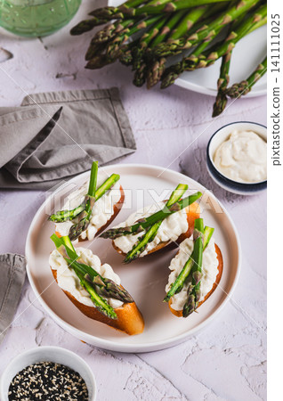 Crispy toasts with cream cheese and asparagus on a plate on the table vertical view Crispy toasts with cream cheese and asparagus on a plate on the table vertical view 141111025