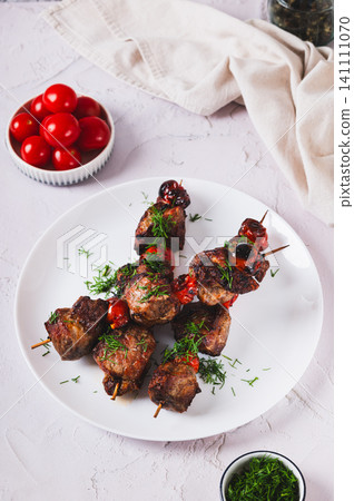 Grilled meat baked in spices with cherry tomatoes on skewers on a plate on the table vertical view Grilled meat baked in spices with cherry tomatoes on skewers on a plate on the table vertical view 141111070