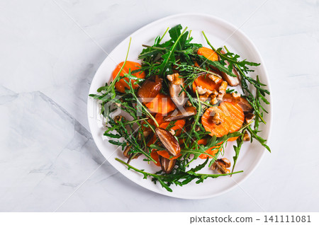 Close up of vegetarian salad with dates, carrots, arugula and nuts on a plate on the table top view Close up of vegetarian salad with dates, carrots, arugula and nuts on a plate on the table top view 141111081