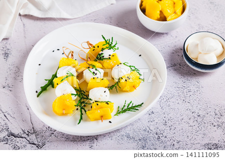 A delicious appetizer of mango, mozzarella, and arugula on a plate on the table A delicious appetizer of mango, mozzarella, and arugula on a plate on the table 141111095
