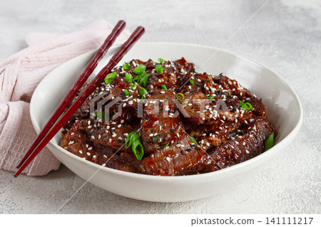 Crispy beef, with green onions and sesame seeds, in a bowl with chopsticks, on a textured surface, on a light background, no people Crispy beef, with green onions and sesame seeds, in a bowl with chopsticks, on a textured surface, on a light background, no people 141111217