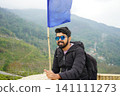 Happy young man wearing sunglasses standing near blue flag at Tinchuley viewpoint in Darjeeling 141111273