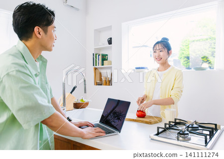 一名男子在廚房查看電子郵件，一名女子在做早餐。 141111274