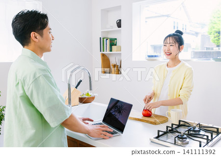 一名男子在廚房查看電子郵件,一名女子在做早餐。 一名男子在廚房查看電子郵件,一名女子在做早餐。 141111392