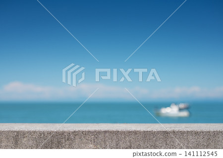 Blurred boat on calm sea behind concrete surface under clear blue sky. 141112545