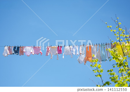 Colorful baby clothes drying on a line under clear blue sky outdoors. Colorful baby clothes drying on a line under clear blue sky outdoors. 141112550