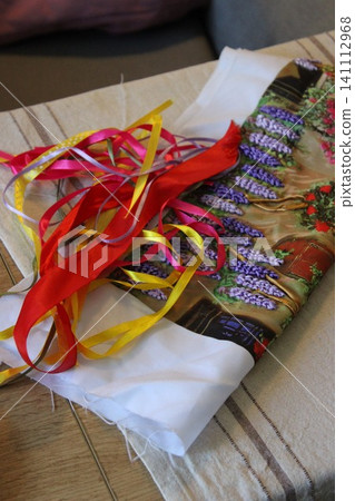 Colorful ribbons in red, yellow, and pink arranged on a fabric with floral design, resting on a wooden table with a striped tablecloth in a cozy indoor setting Colorful ribbons in red, yellow, and pink arranged on a fabric with floral design, resting on a wooden table with a striped tablecloth in a cozy indoor setting 141112968