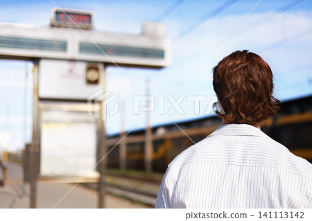 male passenger stands on a train station platform, looking at the departure board. The traveler is waiting for his connection to begin his journey. male passenger stands on a train station platform, looking at the departure board. The traveler is waiting for his connection to begin his journey. 141113142
