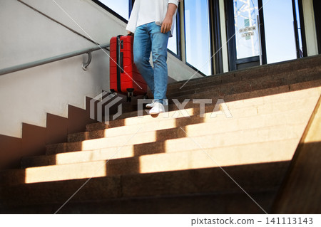 passenger is descending station stairs carrying a red suitcase. Walking down with the luggage, they are ready for travel. passenger is descending station stairs carrying a red suitcase. Walking down with the luggage, they are ready for travel. 141113143