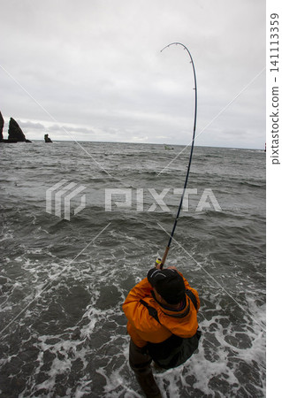 A fisherman in orange clothing enjoys salmon fishing in the sea. 141113359