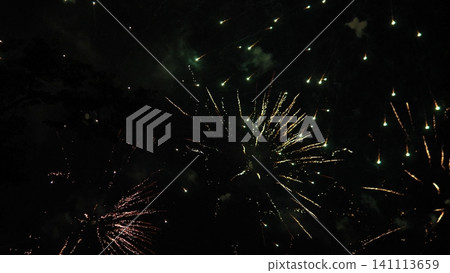 Bright fireworks explode across dark night sky, sending gold, green, and pink streaks outward with smoky haze, scattered sparks, and festive celebratory atmosphere overhead Bright fireworks explode across dark night sky, sending gold, green, and pink streaks outward with smoky haze, scattered sparks, and festive celebratory atmosphere overhead 141113659