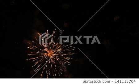 Golden fireworks explode in dark night sky, sending bright radiant trails outward from glowing center with faint smoke clouds and scattered sparks creating dramatic festive scene Golden fireworks explode in dark night sky, sending bright radiant trails outward from glowing center with faint smoke clouds and scattered sparks creating dramatic festive scene 141113704