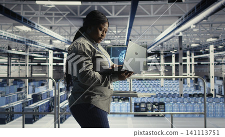 Data center administrator uses a laptop to monitor deep learning processes, working with AI technology and high performance systems. Data center administrator uses a laptop to monitor deep learning processes, working with AI technology and high performance systems. 141113751