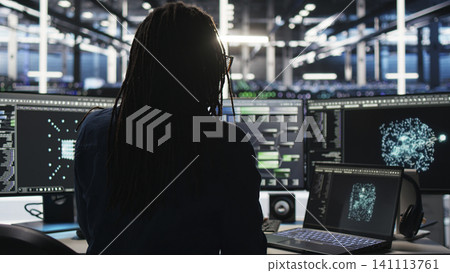 Data center technician arriving in office, working with AI visualization insights on computer to improve system health. Data center technician arriving in office, working with AI visualization insights on computer to improve system health. 141113761