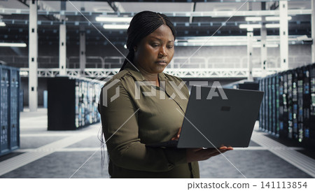 Technical specialist in data center working with notebook computer to update systems for increase in customers workload capacity. Technical specialist in data center working with notebook computer to update systems for increase in customers workload capacity. 141113854