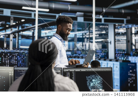 Server room engineer reviewing AI visual analytics dashboard to pinpoint performance problems across server clusters. Server room engineer reviewing AI visual analytics dashboard to pinpoint performance problems across server clusters. 141113908
